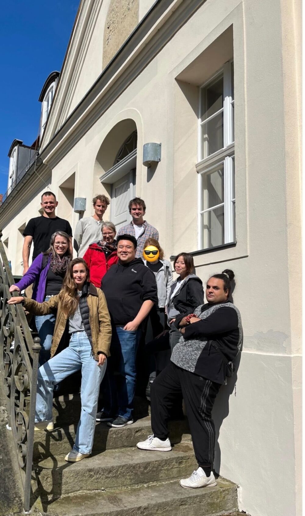 The STF team (ten people) standing on stairs outdoors on a very sunny day at Coconat in Bad Belzig.